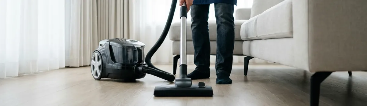 Professional house cleaner vacuuming a living room floor with a canister vacuum cleaner, Dover, DE.