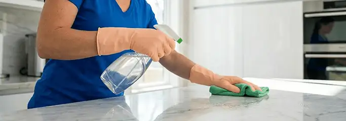 Maid service worker spraying and wiping a kitchen countertop with a microfiber cloth for sanitizing, Dover, DE.
