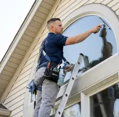 Professional window cleaner on a ladder using a squeegee to clean an exterior arched window, Dover, DE.