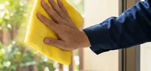 House cleaner wiping a glass window with a yellow microfiber cloth for streak-free cleaning, Dover, DE.